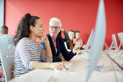 A student and a lecturer sat together working on a computer in a classroom.
