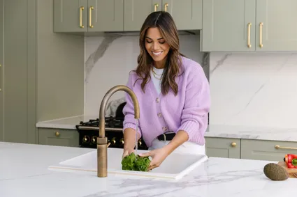 Dr Hazel Wallace standing in a kitchen at the skin washing vegetables under the tap