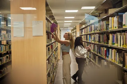 Two students picking out books from a bookshelf in the library.