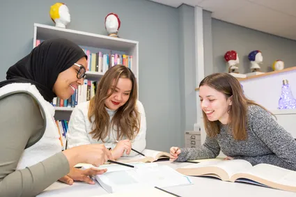 Students smiling and pointing at a text book in the psychology study area.