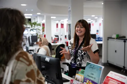 Student speaking with a staff member at a university help desk in a campus support area.