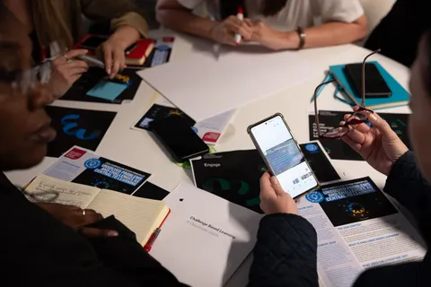 A group of people sat at a table with workbooks and mobile devices