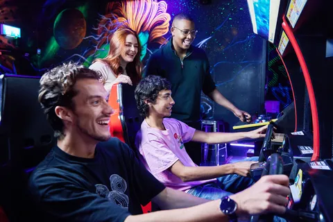 A group of students playing on a racing car game in an arcade bar.