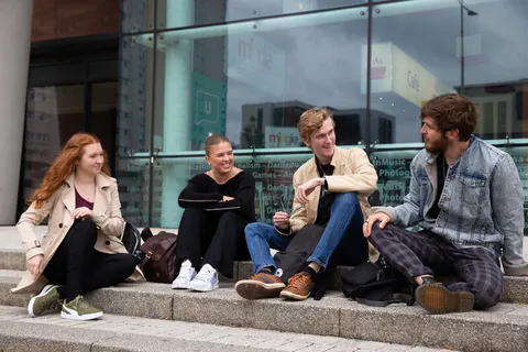 Four students sat on steps outside the Cardiff Campus.