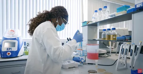 biology student standing in a biology lab using a syringe to move liquid