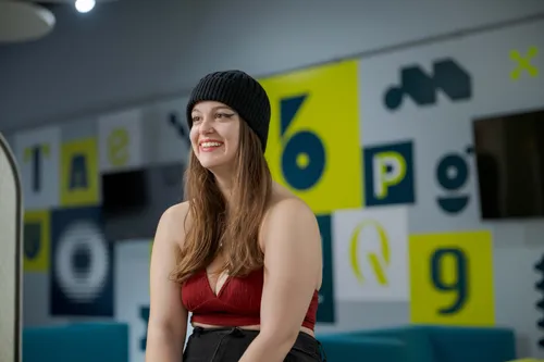 profile shot against a modern indoor background of a smiling advertising student on the Cardiff campus, wearing a black beanie hat and red top