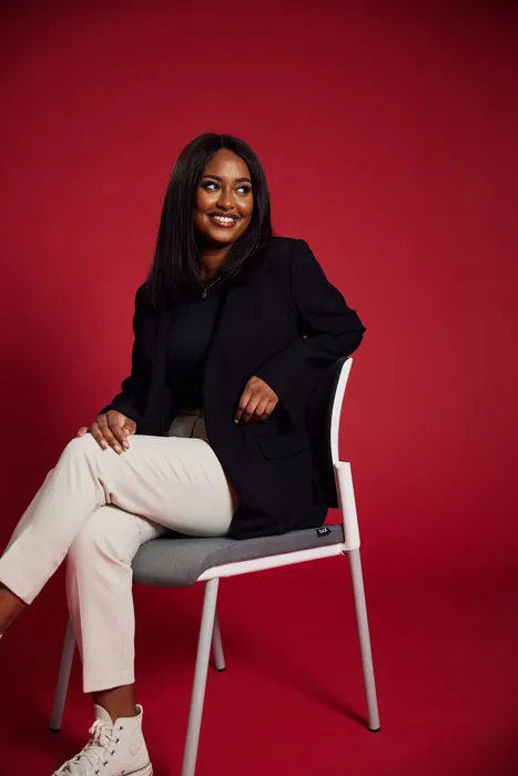 Student Nadifa Saleh sits with their legs crossed on a chair against a red backdrop