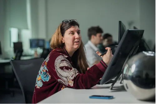 Donna sat in front of a computer and a desk smiling off camera