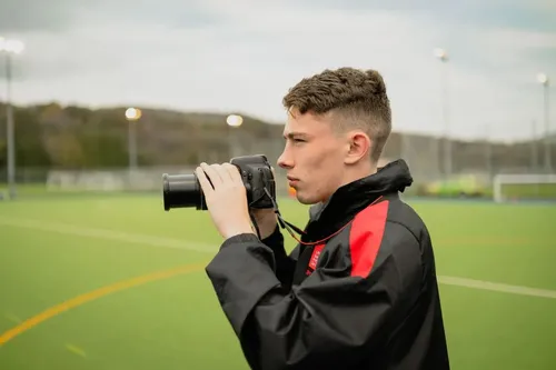 A student in sports journalism photographs a football match with his camera on the pitch