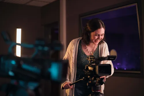 A performance student stands confidently in front of a camera in a studio, ready for filming.