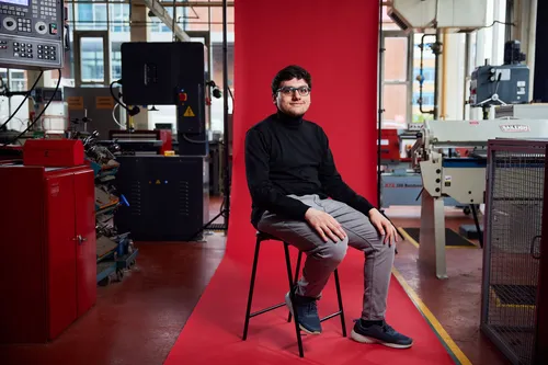 Student Musab Kazi sitting in front of red backdrop with engineering equipment in the background