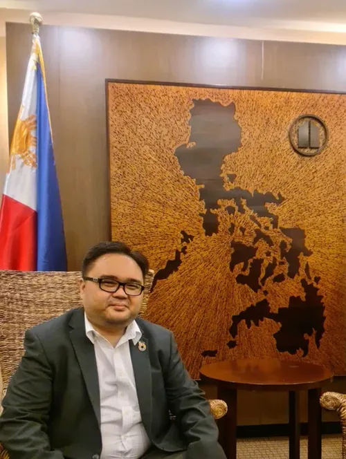 Jonas smiling at the camera with a map and flag of Philippines in the background.