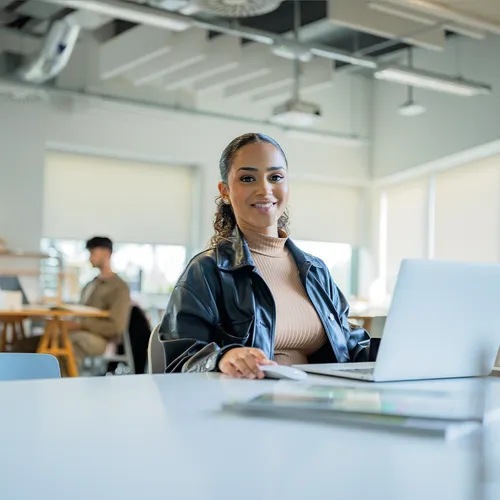 An interior design student working on her laptop in a classroom and smiling at the camera.