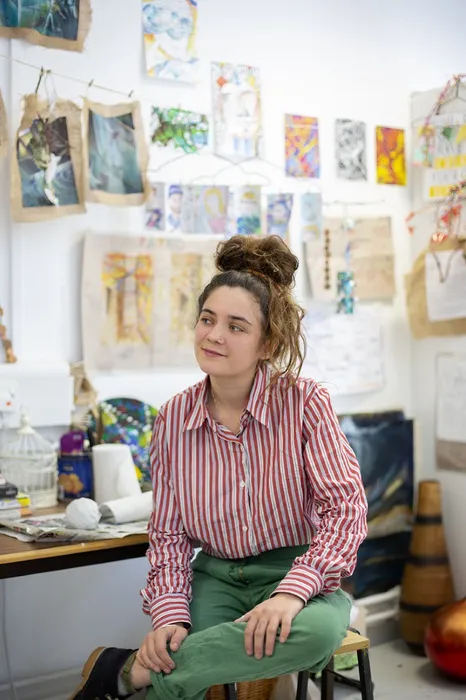 anna coviello sitting in an art studio surrounded by art work