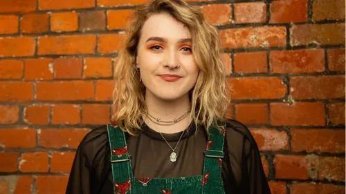 Singer-songwriter Foxxglove smiles for a photo against a brick wall