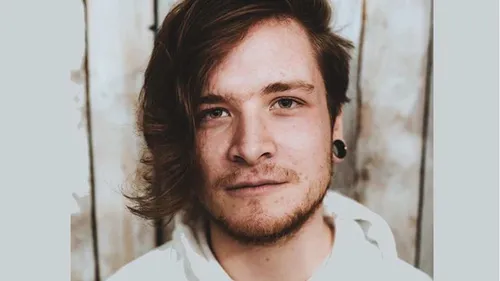 Music graduate, James, looks directly at camera whilst having his photo taken against a white wooden wall