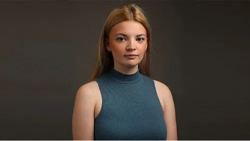 Drama student, Niamh, poses for a headshot photo. She is wearing a blue vest and is looking directly at the camera