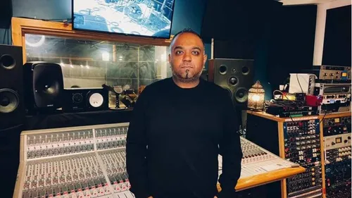 Romesh, grammy-nominated producer, stands proudly in front of a mixing board in a music studio