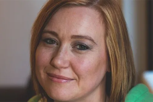 Emma smiles for a photograph, wearing a green jumper