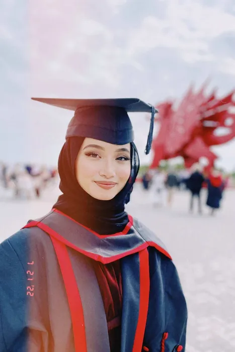 Graduate, Aisyah Mazlan, dressed in graduation gown and hat, stood in front of the Welsh dragon.