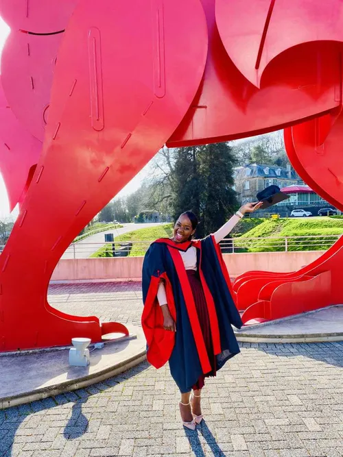 Alumni Gladys poses for a graduation photo in front of the red dragon at ICC Newport