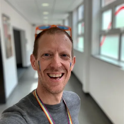 David Sinclair smiles at the camera in a selfie with facepoint on their cheeks and sunglasses on their head in a corridor