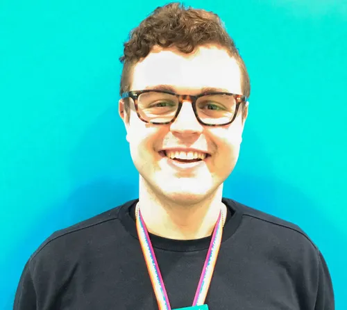 Students wellbeing support officer Jamie Evans smiles at the camera in front of a blue backdrop