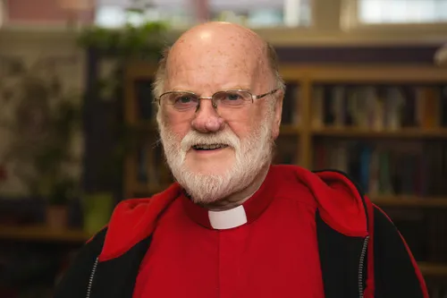 Ray Vincent smiles at the camera while wearing a priest's dog collar in a church