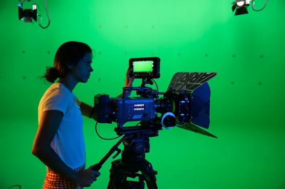 film student using camera equipment in front of green screen