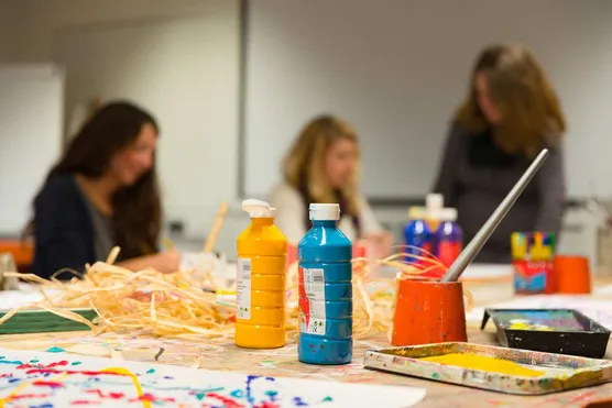 A close up of bottles of paint with students working on their artwork in the background.