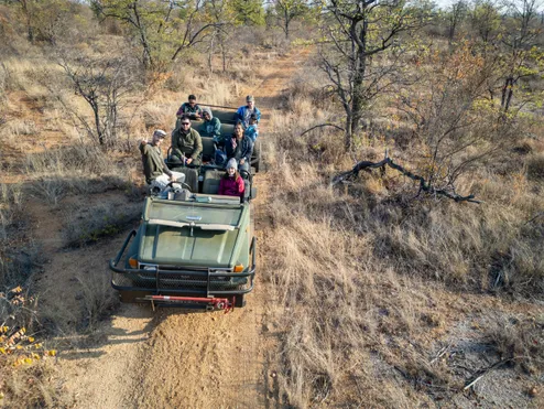 A group of students and academics wearing winter coats and hats smile while on a placement at the camera from a safari car driving in the wilderness of South Africa