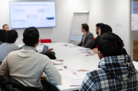 students sitting around a table at business clinic watching presentation on screen