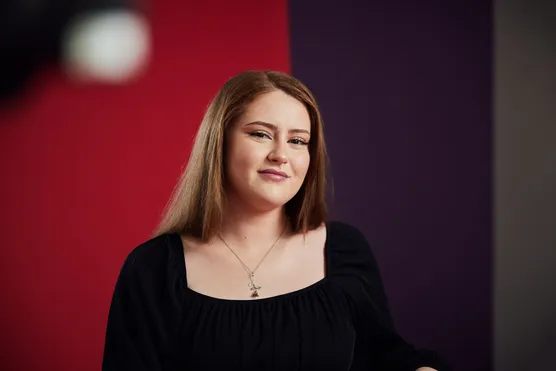 Marketing student Holly Rose Jenkins smiles at the camera in front of a red backdrop