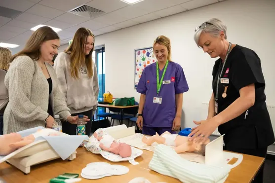 Prospective students and a lecturer in a classroom at Glyntaff Campus, interacting with baby dolls on open day.