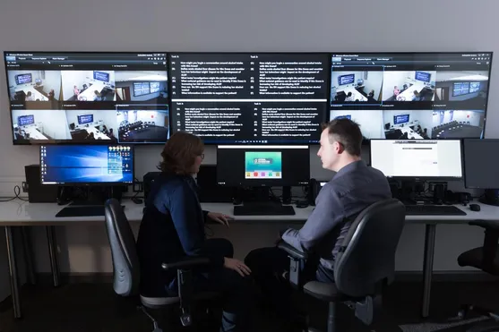Two policing lecturers sat discussing in front of the screens in the hydra simulation centre on glyntaff campus