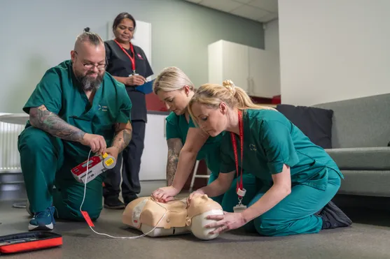 Three students practising CPR on a simulated dummy with a lecturer overseeing