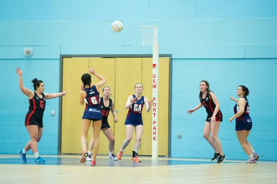 Two teams are playing netball close to the goal.