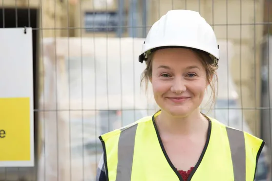 quantity surveyor Anna Chappell standing in front of a building site wearing an hi-vis jacket and hard hat