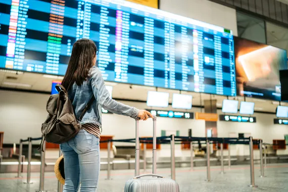 A lady standing looking at the departures board in an airport