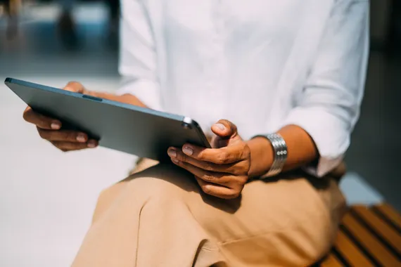 A close up view of a person reading something on a tablet while sitting on the street bench.