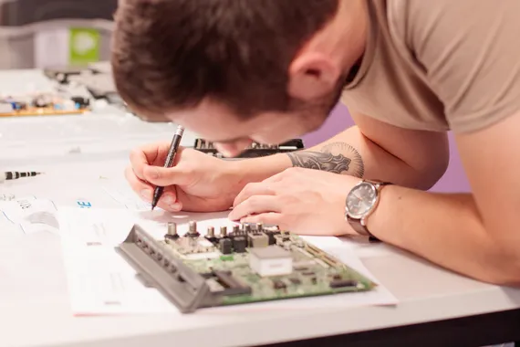 A cyber student making notes next to a computer motherboard.