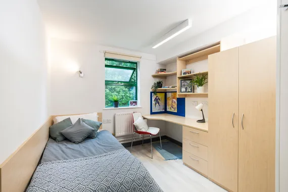 A single room at our Pontypridd accommodation featuring a bed, desk, window and wardrobe.