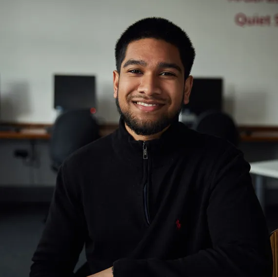 A student smiling at the camera with computer work spaces in the background.