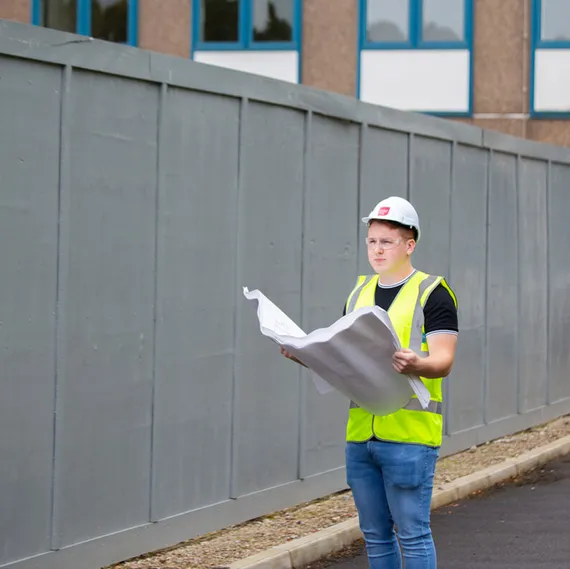 a student wearing a hard hat and a high vis jacket looking at a piece of paper