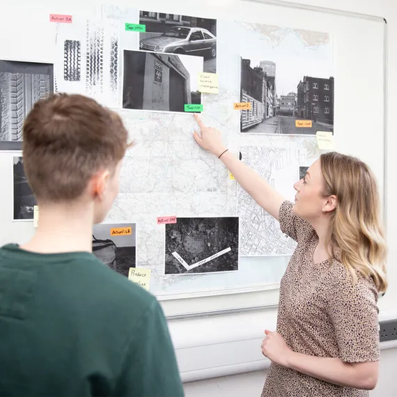 two criminology students standing in front of a whiteboard interrogating crime evidence