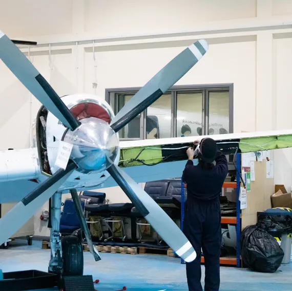 A student in navy overalls carries out maintenance on the front of a small aircraft's wing inside USW's aerospace workshop