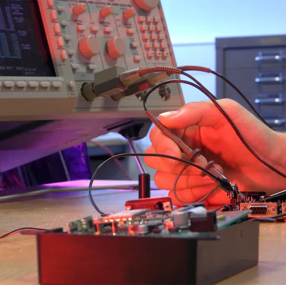 A close up of a student's hand working on electronic equipment with a soldering iron