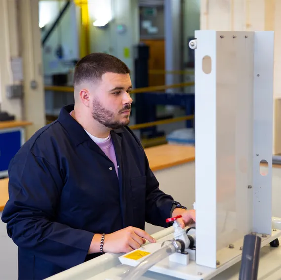 A student in navy overalls uses a piece of mechanical equipment in an engineering workshop