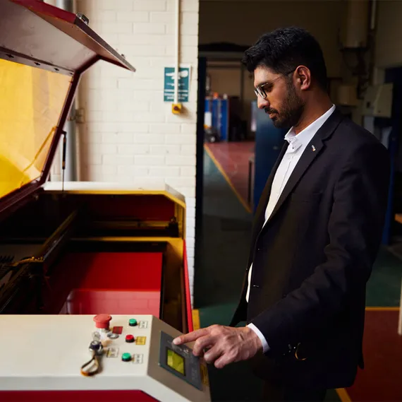 A student dressed in a suit uses a piece of mechanical engineering equipment in a USW Treforest engineering workshop