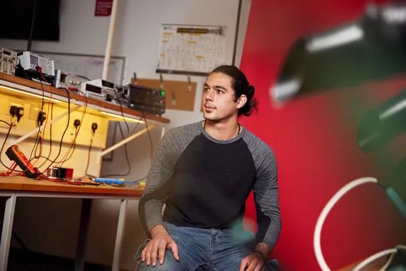 A student sat against a red backdrop surrounded by automotive engineering equipment